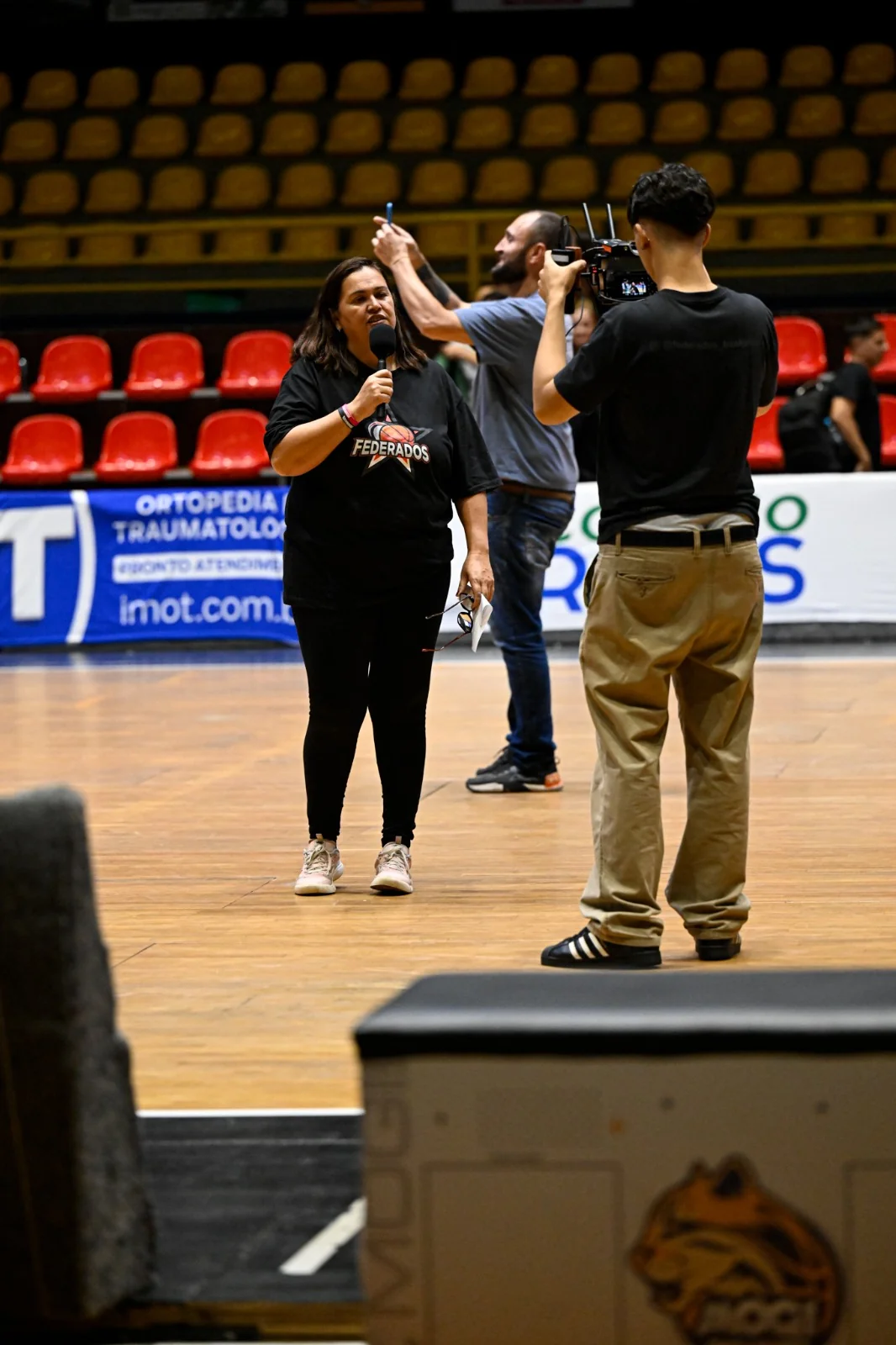 Apresentadora da Federados com microfone e equipe de filmagem trabalhando na quadra